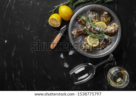 Fresh closed oysters, ice, lemon on a round metal plate and champagne are on a black stone textured background. Top view with copy space. Close-up.