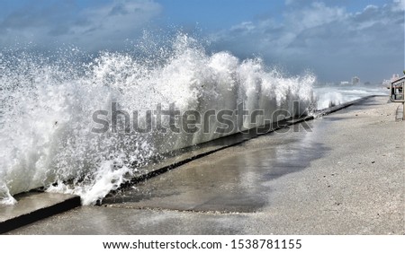 Large wave is crashing into beach wall during a stormy day in a St.Pete Beach n Florida during Nestor showing rising sea levels due to GLobal warning threaten beach goers. Royalty-Free Stock Photo #1538781155