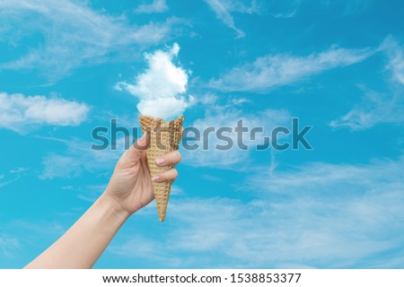 Summer Vacation and Holiday Concept : Woman hand holding Ice cream cone with white cloud with blue sky in background.