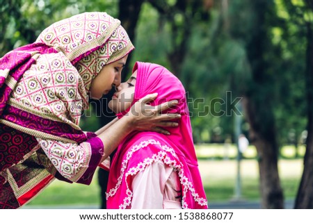 Portrait of happy lovely family arabic muslim mother and little muslim girls child with hijab dress smiling and having fun hugging and kissing together in summer park