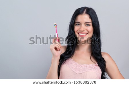 Young woman holding a toothbrush on a gray background
