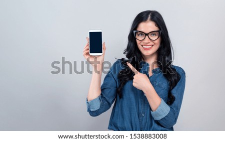 Young woman holding out a cellphone in her hand on a gray background
