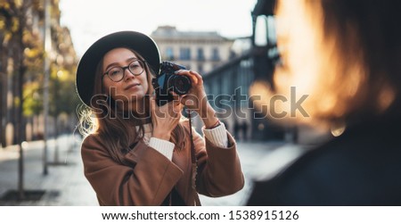 Photographer in glasses with retro camera take photoshoot model girlfriend. Tourist smile girl in hat travels in Barcelona holiday with traveler friend. Sunlight flare street in europe