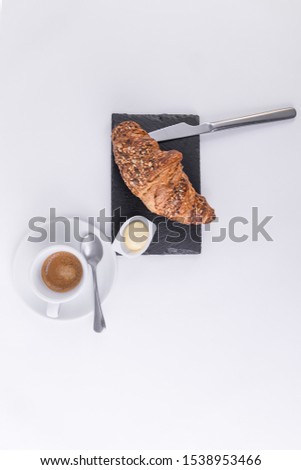 Spreadable butter, a croissant with sesame seeds and a hot coffee on a black cutting board.