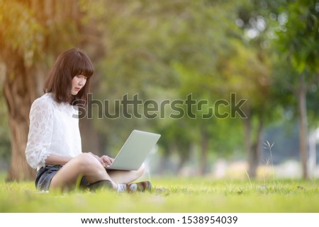 Woman sitting on grass at park  city and working on laptop.