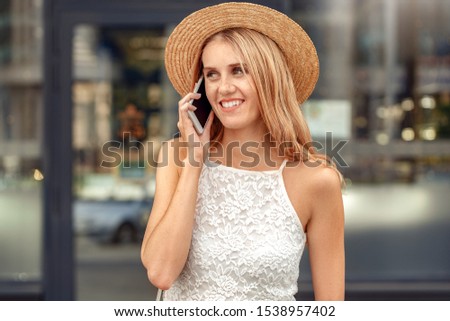 Young girl wearing hat standing on city street talking on smartphone with friend looking aside smiling cheerful close-up