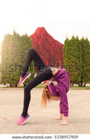 Little girl gymnast doing back bend bent leg up outdoors in the autumn park excited full body shot