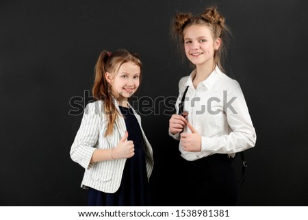 two young pretty school girls are standing , holding papers in their hands and smiling