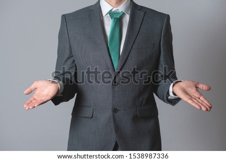 Businessman is spreading his hand aside on gray background. Have no idea.