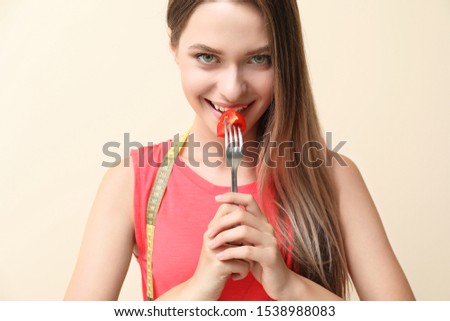 Woman with fresh tomato on fork and measuring tape on light background. Diet concept