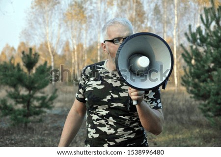 Portrait of a young man screaming with a megaphone in the forest. Lost People Search Concept. Outdoors