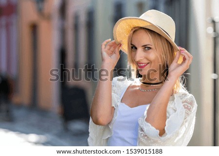 Portrait of beautiful blond woman with sun hat dressed in  light clothes. Trendy girl posing in the street background.