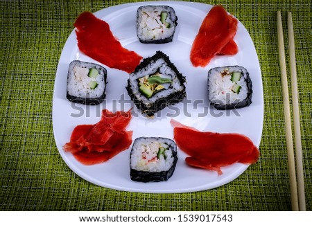 On a green tablecloth in a white plate are rolls with ginger, next to a plate of bamboo sticks
