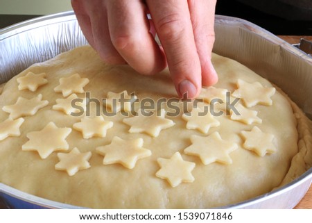 Traditional American homemade Christmas pie. Closeup of man's hands decorating an apple pie dessert with small shortcrust pastry stars