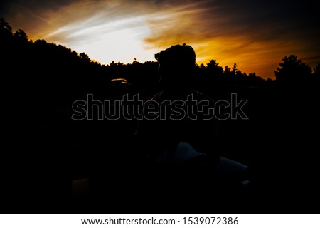 Fashionable handsome man sitting on the bench at park picnic area in the forest looking at the sunset, low key, dark image