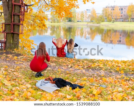 two girls are sitting on the riverbank, and a third girl is photographing them. autumn landscape.