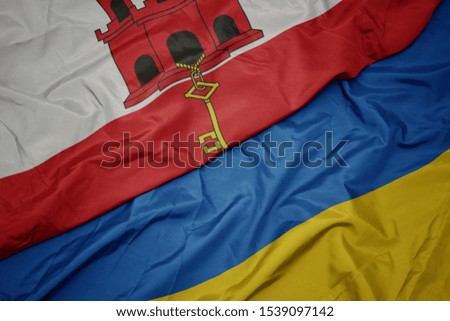 waving colorful flag of ukraine and national flag of gibraltar. macro