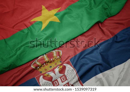 waving colorful flag of serbia and national flag of burkina faso. macro