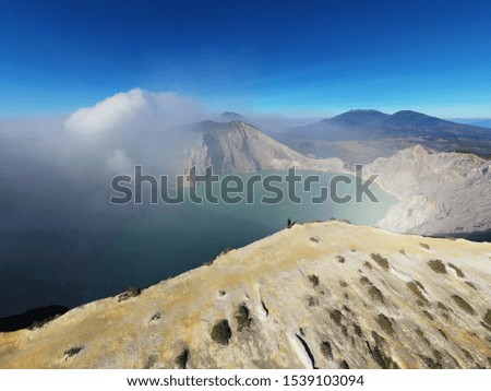 majestic and beautiful aerial travel photo of a traveler standing on the edge of a cliff overlooking Mount Ijen crater in East Java, Indonesia