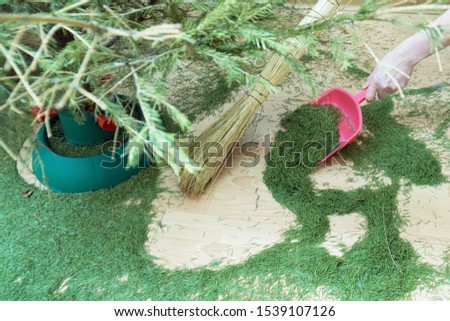 Woman sweeping the floor from dry fallen Christmas tree needles after New Year holidays manually using a broom and a scoop