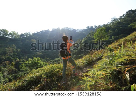Woman hiker taking pictures with smartphone in autumn forest