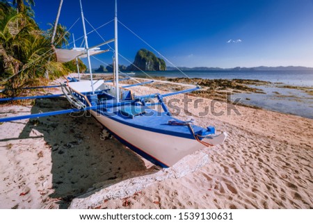 Traditional banca boat at exotic sandy beach with amazing Pinagbuyutan tropical island in background. Exotic nature scenery in El Nido, Palawan, Philippines