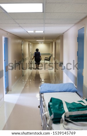 Generic hospital hallway, with a bed waiting for a patient, African nurse walking