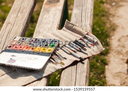 Art palette, watercolors, brushes on a wooden bench outdoors