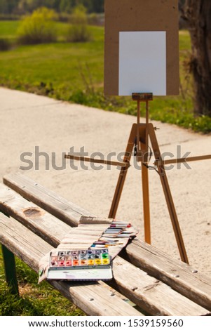 Wooden easel with clean paper and art supplies outdoors