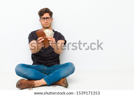 young handsome man with a wallet sitting on the floor sitting on the floor in a white room