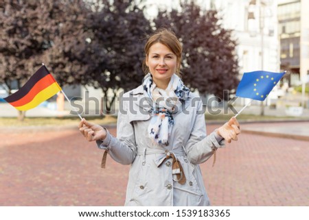 Middle-aged woman with flags of Germany and the European Union against the backdrop of the park and the city.