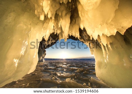 Surreal landscape with people exploring mysterious ice grotto cave. Outdoor adventure. Family exploring huge icy cave, dark majestic landscape. Magical silhouettes on background of illuminated ice