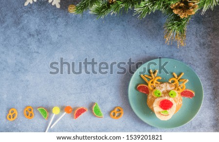 Christmas edible deer of buns and marmalade on a blue plate on the holiday table next to candy, snowflakes and branches of the Christmas tree.Christmas baby food.Christmas minimalism