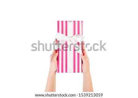 Woman hands give wrapped Christmas or other holiday handmade present in pink paper with white ribbon. Isolated on white background, top view. thanksgiving Gift box concept.