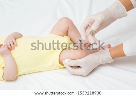 Doctor hands in rubber protective gloves holding syringe. Infant receiving vaccine in leg. Visit to pediatrician at hospital. Two month old baby. Close up.  Royalty-Free Stock Photo #1539218930
