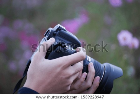 Hand holding SLR (Cosmos field background)