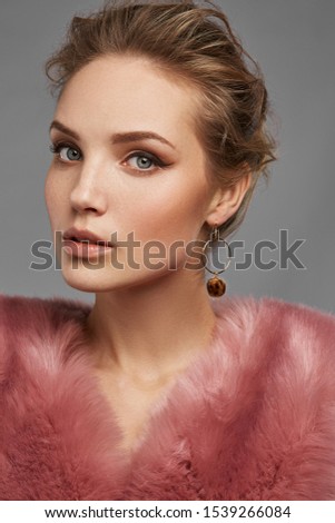 Cropped close-up shot of a brown-haired lady in pink furs wearing stud earrings in the form of the brown fur balls with leopard spots fixed on the golden ring.