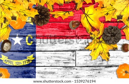 State of North Carolina flag on autumn wooden background with leaves and good place for your text
