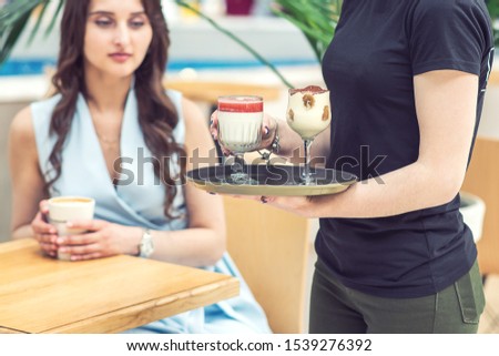 Waiter carries cocktails on tray on background of girl with coffee outdoors close up. Female is carrying the cocktails at cafe outdoors.