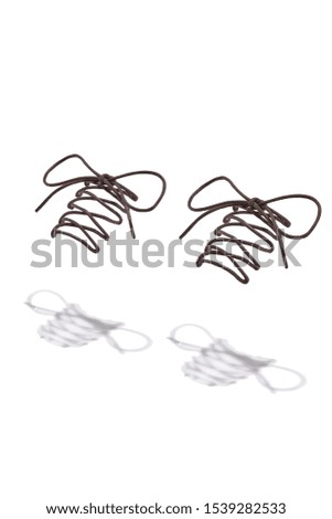 Photo of a pair of dark brown shoelaces tied with a bow hanging in the air and casting a shadow.
The picture was taken in the studio on a white background