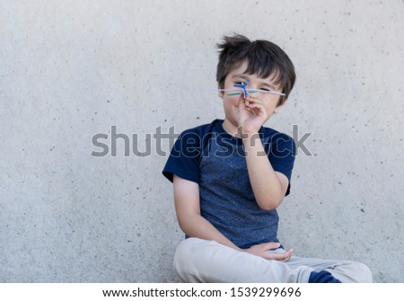 Portrait active little boy playing with toy airplane against gray concrete  background, Child throwing foam airplane, Kid playing in the park,  Childhood outdoor activity concept.