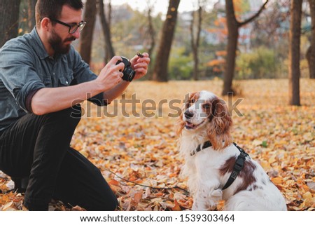 Man photographing his dog in a park. Male person taking picture of his well-trained pet