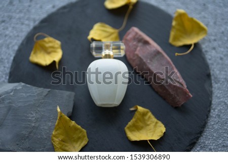 white perfume bottle with yellow autumn leaves and stones on a black round stone plate