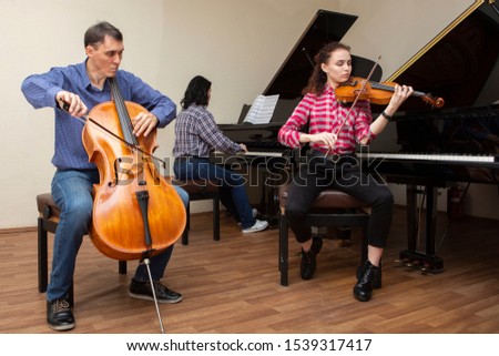 Family trio rehearsing. Father plays the cello, daughter is a violinist, mother plays the piano. Portrait.