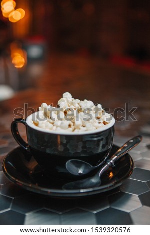 Mug of cappuccino coffee with popcorn on a bar counter in the light of colored lamps. The cup is black. Mosaic table. Cocoa. Great background for Photoshop, suitable in the menu.