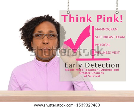 Woman looking at camera with fat marker writing on Think Pink Early Detection Means More Treatment Options and Greater Chances of Survival Sign hanging over wood countertop