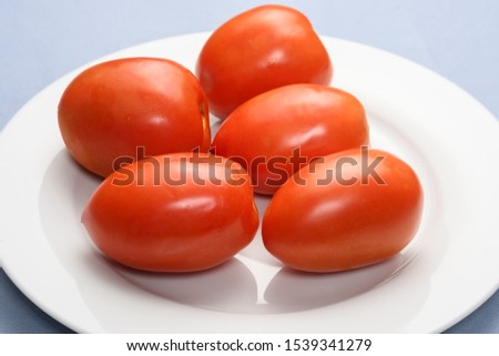 RED TOMATOES ON A WHITE PLATE ON A LIGHT BLUE BACKGROUND