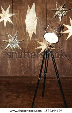 Vintage chrome tripod spotlight and stars ligths on brown wood wall, copy space. Floor lamp, lampshade. Christmas background