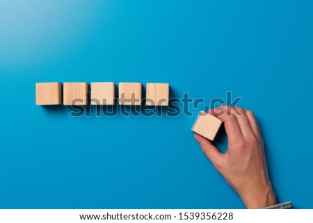 Woman's hand establishes a wooden cubes in row. Blank wooden blocks for word, text or illustration. Hand placing cube and finishing the row