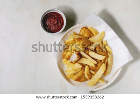 Classic british fast food fish and chips served on white paper in plate with red ketchup sauce over white marble background. Flat lay, space